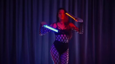 Elinde fenerlerle dans eden seksi bir kadın. Bir dansçı kız karanlık bir salonda erotik bir şekilde dans eder. Yavaş çekim. Twerk, yüksek topuklar, striptiz, baştan çıkarıcı bir dans. Balık ağı çoraplı bir kadın ahşap zeminde boğucu bir poz veriyor..
