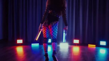 Elinde fenerlerle dans eden seksi bir kadın. Bir dansçı kız karanlık bir salonda erotik bir şekilde dans eder. Yavaş çekim. Twerk, yüksek topuklar, striptiz, baştan çıkarıcı bir dans. Balık ağı çoraplı bir kadın ahşap zeminde boğucu bir poz veriyor..