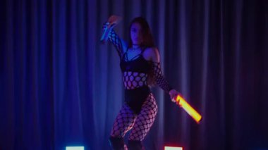 Elinde fenerlerle dans eden seksi bir kadın. Bir dansçı kız karanlık bir salonda erotik bir şekilde dans eder. Yavaş çekim. Twerk, yüksek topuklar, striptiz, baştan çıkarıcı bir dans. Balık ağı çoraplı bir kadın ahşap zeminde boğucu bir poz veriyor..