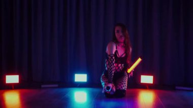 Elinde fenerlerle dans eden seksi bir kadın. Bir dansçı kız karanlık bir salonda erotik bir şekilde dans eder. Yavaş çekim. Twerk, yüksek topuklar, striptiz, baştan çıkarıcı bir dans. Balık ağı çoraplı bir kadın ahşap zeminde boğucu bir poz veriyor..
