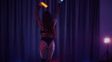 Elinde fenerlerle dans eden seksi bir kadın. Bir dansçı kız karanlık bir salonda erotik bir şekilde dans eder. Yavaş çekim. Twerk, yüksek topuklar, striptiz, baştan çıkarıcı bir dans. Balık ağı çoraplı bir kadın ahşap zeminde boğucu bir poz veriyor..