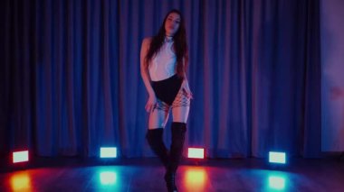Yüksek topuklularla dans eden seksi kadın. Yavaş çekim. Bir dansçı kız karanlık bir salonda erotik bir şekilde dans eder. Twerk, yüksek topuklar, striptiz, baştan çıkarıcı bir dans. Atmosferik renkli ışık, kulüp, sahne. Balık ağı çoraplı baştan çıkarıcı kadın yerde poz veriyor.. 