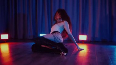 Yüksek topuklularla dans eden seksi kadın. Yavaş çekim. Bir dansçı kız karanlık bir salonda erotik bir şekilde dans eder. Twerk, yüksek topuklar, striptiz, baştan çıkarıcı bir dans. Atmosferik renkli ışık, kulüp, sahne. Balık ağı çoraplı baştan çıkarıcı kadın yerde poz veriyor.. 