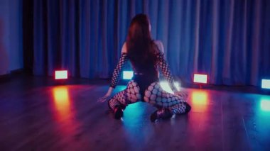Dans eden seksi kadın twerk. Bir dansçı kız karanlık bir salonda erotik bir şekilde dans eder. Yavaş çekim. Twerk, yüksek topuklar, striptiz, baştan çıkarıcı bir dans. Atmosferik renkli ışık, kulüp, sahne. Balık ağı çoraplı bir kadın yerde boğucu bir poz veriyor..