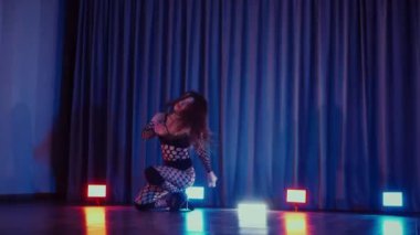 Dans eden seksi kadın twerk. Bir dansçı kız karanlık bir salonda erotik bir şekilde dans eder. Yavaş çekim. Twerk, yüksek topuklar, striptiz, baştan çıkarıcı bir dans. Atmosferik renkli ışık, kulüp, sahne. Balık ağı çoraplı bir kadın yerde boğucu bir poz veriyor..