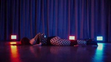 Dans eden seksi kadın twerk. Bir dansçı kız karanlık bir salonda erotik bir şekilde dans eder. Yavaş çekim. Twerk, yüksek topuklar, striptiz, baştan çıkarıcı bir dans. Atmosferik renkli ışık, kulüp, sahne. Balık ağı çoraplı bir kadın yerde boğucu bir poz veriyor..