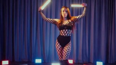 Elinde fenerlerle dans eden seksi bir kadın. Bir dansçı kız karanlık bir salonda erotik bir şekilde dans eder. Yavaş çekim. Twerk, yüksek topuklar, striptiz, baştan çıkarıcı bir dans. Balık ağı çoraplı bir kadın ahşap zeminde boğucu bir poz veriyor..
