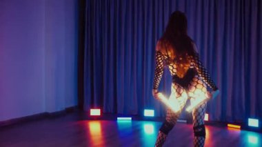 Elinde fenerlerle dans eden seksi bir kadın. Bir dansçı kız karanlık bir salonda erotik bir şekilde dans eder. Yavaş çekim. Twerk, yüksek topuklar, striptiz, baştan çıkarıcı bir dans. Balık ağı çoraplı bir kadın ahşap zeminde boğucu bir poz veriyor..