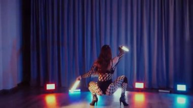 Elinde fenerlerle dans eden seksi bir kadın. Bir dansçı kız karanlık bir salonda erotik bir şekilde dans eder. Yavaş çekim. Twerk, yüksek topuklar, striptiz, baştan çıkarıcı bir dans. Balık ağı çoraplı bir kadın ahşap zeminde boğucu bir poz veriyor..
