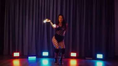 Elinde fenerlerle dans eden seksi bir kadın. Bir dansçı kız karanlık bir salonda erotik bir şekilde dans eder. Yavaş çekim. Twerk, yüksek topuklar, striptiz, baştan çıkarıcı bir dans. Balık ağı çoraplı bir kadın ahşap zeminde boğucu bir poz veriyor..