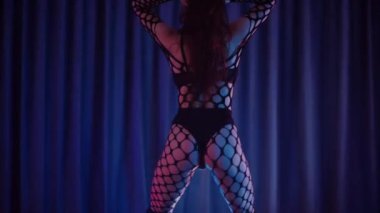 Dans eden seksi kadın twerk. Bir dansçı kız karanlık bir salonda erotik bir şekilde dans eder. Yavaş çekim. Twerk, yüksek topuklar, striptiz, baştan çıkarıcı bir dans. Atmosferik renkli ışık, kulüp, sahne. Balık ağı çoraplı bir kadın yerde boğucu bir poz veriyor..
