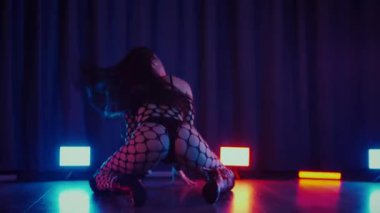 Dans eden seksi kadın twerk. Bir dansçı kız karanlık bir salonda erotik bir şekilde dans eder. Yavaş çekim. Twerk, yüksek topuklar, striptiz, baştan çıkarıcı bir dans. Atmosferik renkli ışık, kulüp, sahne. Balık ağı çoraplı bir kadın yerde boğucu bir poz veriyor..