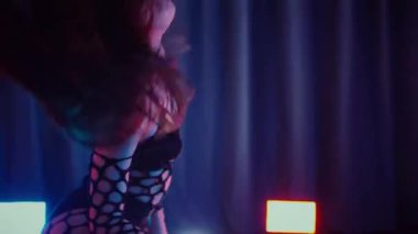 Dans eden seksi kadın twerk. Bir dansçı kız karanlık bir salonda erotik bir şekilde dans eder. Yavaş çekim. Twerk, yüksek topuklar, striptiz, baştan çıkarıcı bir dans. Atmosferik renkli ışık, kulüp, sahne. Balık ağı çoraplı bir kadın yerde boğucu bir poz veriyor..