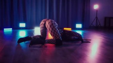 Dans eden seksi kadın twerk. Bir dansçı kız karanlık bir salonda erotik bir şekilde dans eder. Yavaş çekim. Twerk, yüksek topuklar, striptiz, baştan çıkarıcı bir dans. Atmosferik renkli ışık, kulüp, sahne. Balık ağı çoraplı bir kadın yerde boğucu bir poz veriyor..