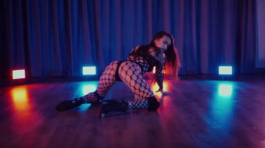 Dans eden seksi kadın twerk. Bir dansçı kız karanlık bir salonda erotik bir şekilde dans eder. Yavaş çekim. Twerk, yüksek topuklar, striptiz, baştan çıkarıcı bir dans. Atmosferik renkli ışık, kulüp, sahne. Balık ağı çoraplı bir kadın yerde boğucu bir poz veriyor..