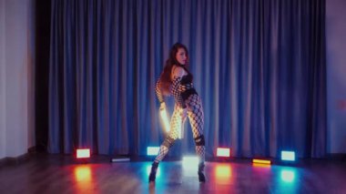 Elinde fenerlerle dans eden seksi bir kadın. Bir dansçı kız karanlık bir salonda erotik bir şekilde dans eder. Yavaş çekim. Twerk, yüksek topuklar, striptiz, baştan çıkarıcı bir dans. Balık ağı çoraplı bir kadın ahşap zeminde boğucu bir poz veriyor..