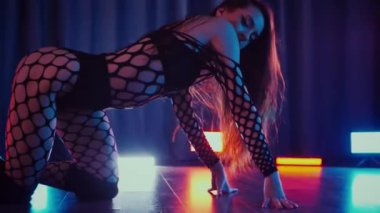 Dans eden seksi kadın twerk. Bir dansçı kız karanlık bir salonda erotik bir şekilde dans eder. Yavaş çekim. Twerk, yüksek topuklar, striptiz, baştan çıkarıcı bir dans. Atmosferik renkli ışık, kulüp, sahne. Balık ağı çoraplı bir kadın yerde boğucu bir poz veriyor..