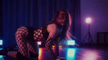 Dans eden seksi kadın twerk. Bir dansçı kız karanlık bir salonda erotik bir şekilde dans eder. Yavaş çekim. Twerk, yüksek topuklar, striptiz, baştan çıkarıcı bir dans. Atmosferik renkli ışık, kulüp, sahne. Balık ağı çoraplı bir kadın yerde boğucu bir poz veriyor..