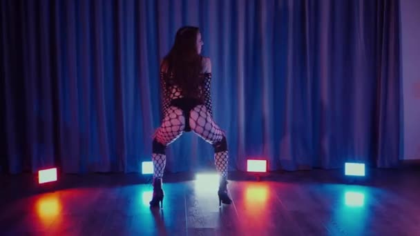 性感的女人在跳舞 一个跳舞的女孩在黑暗的大厅里色情地跳舞 慢镜头拍摄 紧身衣 高跟鞋 脱衣舞 迷人的舞蹈大气彩灯 俱乐部 一个穿着鱼网袜的女人在地板上摆出不雅的姿势 — 图库视频影像