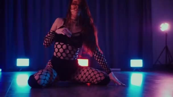 性感的女人在跳舞 一个跳舞的女孩在黑暗的大厅里色情地跳舞 慢镜头拍摄 紧身衣 高跟鞋 脱衣舞 迷人的舞蹈大气彩灯 俱乐部 一个穿着鱼网袜的女人在地板上摆出不雅的姿势 — 图库视频影像