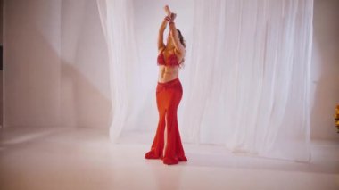 Güzel kız oryantal göbek dansı yapıyor. Kırmızı iç çamaşırlı seksi kadın beyaz bir stüdyoda baştan çıkarıcı bir dans yapıyor. Güzel bir karın ve göğüsler. Kırmızı elbiseli şık bir kadın model. Kırmızı elbiseli zarif bir kadın poz veriyor.. 