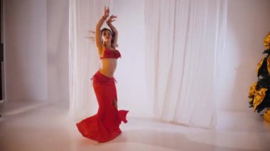 Güzel kız oryantal göbek dansı yapıyor. Kırmızı iç çamaşırlı seksi kadın beyaz bir stüdyoda baştan çıkarıcı bir dans yapıyor. Güzel bir karın ve göğüsler. Kırmızı elbiseli şık bir kadın model. Kırmızı elbiseli zarif bir kadın poz veriyor.. 