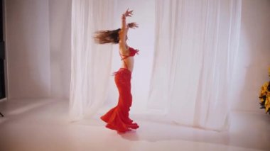 Güzel kız oryantal göbek dansı yapıyor. Kırmızı iç çamaşırlı seksi kadın beyaz bir stüdyoda baştan çıkarıcı bir dans yapıyor. Güzel bir karın ve göğüsler. Kırmızı elbiseli şık bir kadın model. Kırmızı elbiseli zarif bir kadın poz veriyor.. 