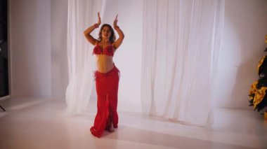 Güzel kız oryantal göbek dansı yapıyor. Ağır çekim. Kırmızı iç çamaşırlı seksi kadın beyaz bir stüdyoda baştan çıkarıcı bir dans yapıyor. Güzel bir karın ve göğüsler. Kırmızı elbiseli şık bir kadın model. Kırmızı elbiseli zarif bir kadın poz veriyor.. 