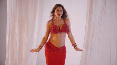 Güzel kız oryantal göbek dansı yapıyor. Ağır çekim. Kırmızı iç çamaşırlı seksi kadın beyaz bir stüdyoda baştan çıkarıcı bir dans yapıyor. Güzel bir karın ve göğüsler. Kırmızı elbiseli şık bir kadın model. Kırmızı elbiseli zarif bir kadın poz veriyor.. 
