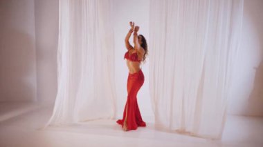 Güzel kız oryantal göbek dansı yapıyor. Ağır çekim. Kırmızı iç çamaşırlı seksi kadın beyaz bir stüdyoda baştan çıkarıcı bir dans yapıyor. Güzel bir karın ve göğüsler. Kırmızı elbiseli şık bir kadın model. Kırmızı elbiseli zarif bir kadın poz veriyor.. 
