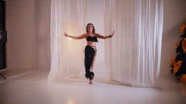 Güzel kız oryantal göbek dansı yapıyor. Siyah iç çamaşırlı seksi bir kadın beyaz bir stüdyoda baştan çıkarıcı bir dans yapıyor. Güzel bir karın ve göğüs. Siyah elbiseli zarif bir kadın zarif bir şekilde dans ediyor. Siyah elbiseli büyüleyici dansçı.. 