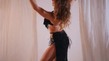 Güzel kız oryantal göbek dansı yapıyor. Siyah iç çamaşırlı seksi bir kadın beyaz bir stüdyoda baştan çıkarıcı bir dans yapıyor. Güzel bir karın ve göğüs. Siyah elbiseli zarif bir kadın zarif bir şekilde dans ediyor. Siyah elbiseli büyüleyici dansçı.. 