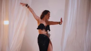 Güzel kız oryantal göbek dansı yapıyor. Siyah göbek dansı kostümlü kadın poz veriyor. Büyüleyici siyah elbiseli kadın dansçı. Koyu renk dansçı kıyafeti içinde zarif bir dansçı. Çarpıcı siyah bir göbek dansı kostümü giymiş bir kadın. yavaş çekim