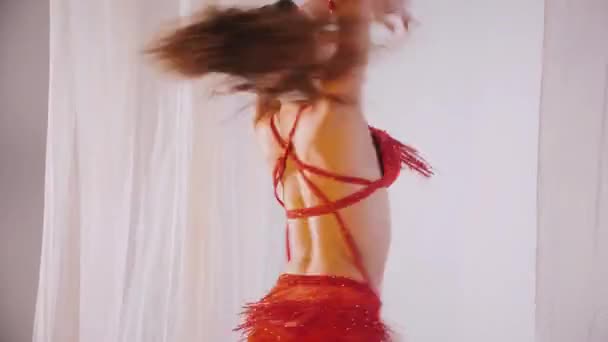美丽的姑娘跳东方式肚皮舞 穿着红色内衣的性感女人正在一个白色工作室里跳着迷人的舞步 漂亮的肚子和乳房 穿着红色衣服的时髦女模特 穿着红色衣服摆姿势的优雅女人 — 图库视频影像