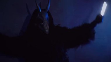 Şeytan canavar elinde RGB çubuklarıyla dans ediyor. Karanlık bir stüdyoda maskeli gizemli bir adam. Adam siyah bir ceket ve boynuzlu bir maske giymiş. Uzaylı uzaylı. Korkunç.,