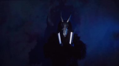 Şeytan canavar elinde RGB çubuklarıyla dans ediyor. Karanlık bir stüdyoda maskeli gizemli bir adam. Adam siyah bir ceket ve boynuzlu bir maske giymiş. Uzaylı uzaylı. Korkunç.,