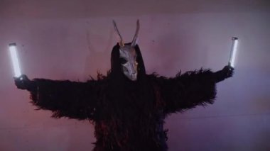 Şeytan canavar elinde RGB çubuklarıyla dans ediyor. Karanlık bir stüdyoda maskeli gizemli bir adam. Adam siyah bir ceket ve boynuzlu bir maske giymiş. Uzaylı uzaylı. Korkunç.,