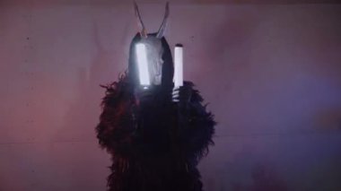 Şeytan canavar elinde RGB çubuklarıyla dans ediyor. Karanlık bir stüdyoda maskeli gizemli bir adam. Adam siyah bir ceket ve boynuzlu bir maske giymiş. Uzaylı uzaylı. Korkunç.,