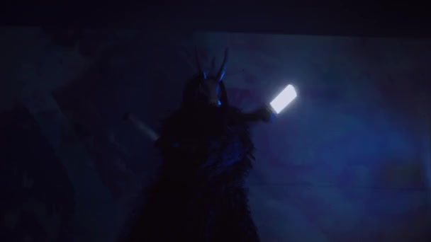 魔鬼带着Rgb跳舞 手里拿着棍子 一个戴着可怕面具的神秘男人在黑暗的工作室里这个男人穿着一件黑色外套 头上戴着一副有角的面具 来自太空的外星人可怕的事 — 图库视频影像