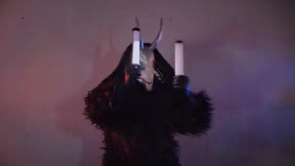悪魔の怪物がRgbで踊っている 暗いスタジオで恐ろしい仮面の神秘的な男 男は黒いコートと頭に角のあるマスクを着ている 宇宙からのエイリアン ホラー — ストック動画