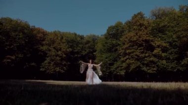 Ormanda göbek dansı yapan bir kız. Doğulu dansı. Beyaz göbek dansı kostümlü kadın sahada hareketlerle poz veriyor. Beyaz kostümlü zarif bir dansçı. Beyaz elbiseli kadın güzel bir açık havada göbek dansı hareketleri sergiliyor.