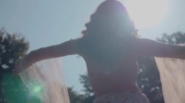 Ormanda göbek dansı yapan bir kız. Doğulu dansı. Beyaz göbek dansı kostümlü kadın sahada hareketlerle poz veriyor. Beyaz kostümlü zarif bir dansçı. Beyaz elbiseli kadın güzel bir açık havada göbek dansı hareketleri sergiliyor.