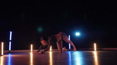 Baştan çıkarıcı dans eden seksi kadın. Erotik bir dansçı kız. Twerk, yüksek topuklu ayakkabı, striptiz. Neon ışıklarla çevrili yerde yatan bir kadın. Canlı neon ışıklarının altında yerde dinlenen bir kadın. Bikinili kadın çömelme egzersizi yapıyor. 