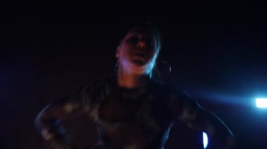 Baştan çıkarıcı dans eden seksi kadın. Erotik bir dansçı kız. Twerk, yüksek topuklu ayakkabı, striptiz. Neon ışıklarla çevrili yerde yatan bir kadın. Canlı neon ışıklarının altında yerde dinlenen bir kadın. Bikinili kadın çömelme egzersizi yapıyor. 