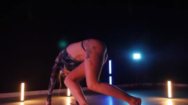 Baştan çıkarıcı dans eden seksi kadın. Erotik bir dansçı kız. Twerk, yüksek topuklu ayakkabı, striptiz. Neon ışıklarla çevrili yerde yatan bir kadın. Canlı neon ışıklarının altında yerde dinlenen bir kadın. Bikinili kadın çömelme egzersizi yapıyor. 
