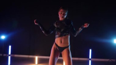 Baştan çıkarıcı dans eden seksi kadın. Erotik bir dansçı kız. Twerk, yüksek topuklu ayakkabı, striptiz. Neon ışıklarla çevrili yerde yatan bir kadın. Canlı neon ışıklarının altında yerde dinlenen bir kadın. Bikinili kadın çömelme egzersizi yapıyor. 