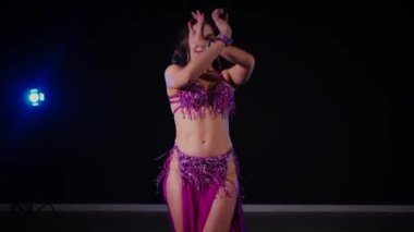 Mor elbiseli kadın loş ışıklı odada zarif bir şekilde göbek dansı yapıyor. Zarif giyimli kadın, müziğe gidiyor ve karanlık ortamda dans ediyor. Gölgeli alanda mor elbiseler giyen kadın dansçı. Karanlık odada dönen bir kadın. 