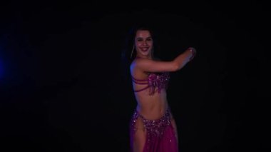 Mor elbiseli kadın loş ışıklı odada zarif bir şekilde göbek dansı yapıyor. Zarif giyimli kadın, müziğe gidiyor ve karanlık ortamda dans ediyor. Gölgeli alanda mor elbiseler giyen kadın dansçı. Karanlık odada dönen bir kadın. 