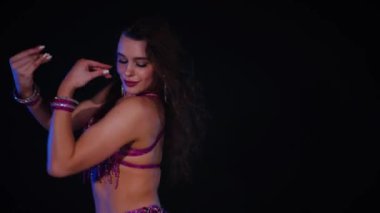 Mor elbiseli kadın loş ışıklı odada zarif bir şekilde göbek dansı yapıyor. Zarif giyimli kadın, müziğe gidiyor ve karanlık ortamda dans ediyor. Gölgeli alanda mor elbiseler giyen kadın dansçı. Karanlık odada dönen bir kadın. 