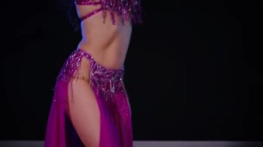 Mor elbiseli kadın loş ışıklı odada zarif bir şekilde göbek dansı yapıyor. Zarif giyimli kadın, müziğe gidiyor ve karanlık ortamda dans ediyor. Gölgeli alanda mor elbiseler giyen kadın dansçı. Karanlık odada dönen bir kadın. 